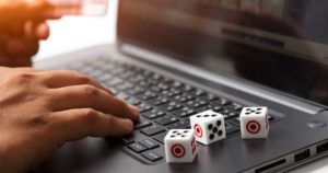 Kädet läppärillä, läppärin päällä kolme noppaa. Toisessa kädessä maksukortti.