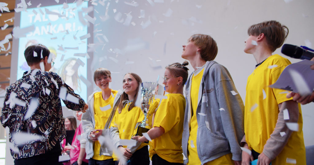 Taloussankari-kilpailun viisihenkinen voittajajoukkue vastaanottaa palkintopokaalia konfettisateessa.