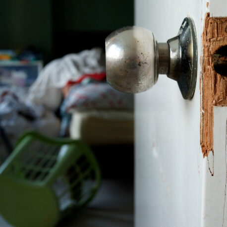 Kuvassa ovi, jossa murron jälkiä. Taustalla huone, jossa tavarat hujan hajan.