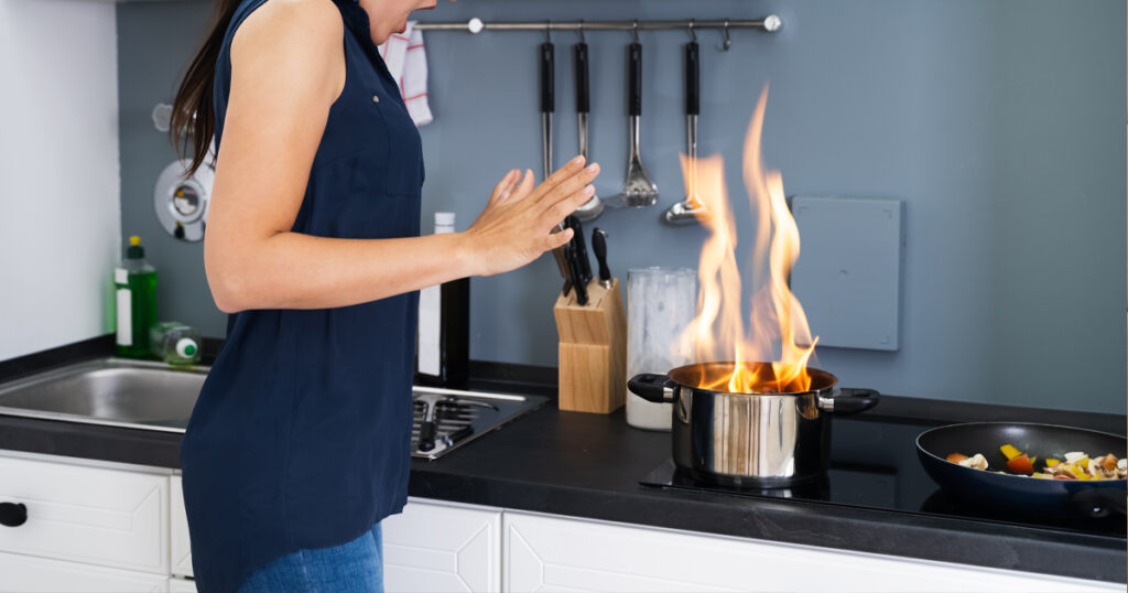 Ihminen seisoo lieden äärellä, jossa kattila ja siellä liekkejä.